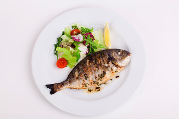 baked whole fish grilled on a plate with vegetables and lemon