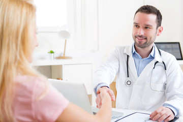 Young attractive doctor shaking hand of his patient