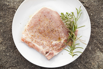 Raw steak on white plate with herbs