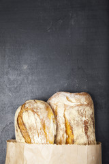 Fresh French cracked bread in a paper bag on a dark background