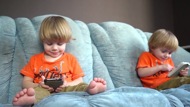 Kids twins having fun playing with mobile cell phones on a couch
