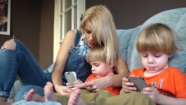 Mother and little sons twins on couch with mobile phones playing