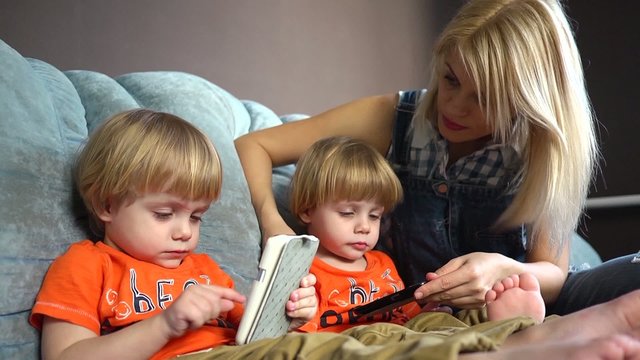 Mother and little sons twins on couch with mobile phones playing
