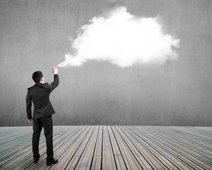 Businessman spraying white cloud paint on gray concrete wall