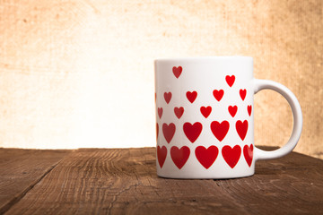 White mug with hearts on old wooden table against the background