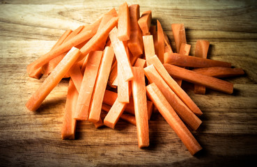 A bunch of pieces of carrots on a wooden cutting board. Toned