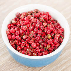 Pink Peppercorns - Bowl with dried pink peppercorns on a wooden background.