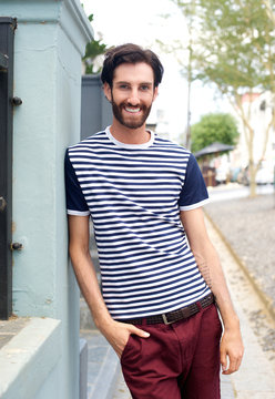 Happy trendy man in striped shirt leaning against wall outdoors