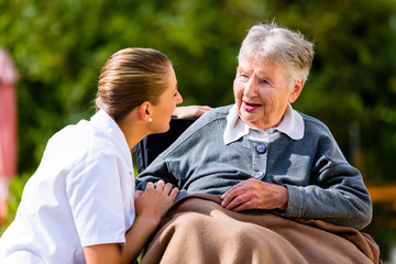 Pflegerin hält Hand alter Frau im Rollstuhl