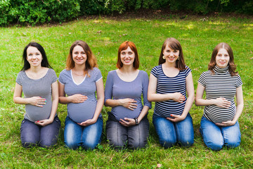 Group of pregnant women sitting on a grass and touching their