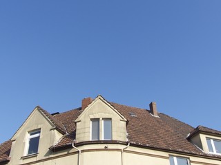 Dachgauben und Mansarden eines alten Eckhaus in Beige und Naturfarben vor blauem Himmel im...