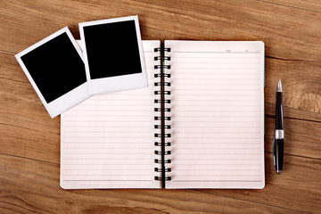 Spiral notebook or photo album with blank polaroid style frame prints laying on a wood desk or table