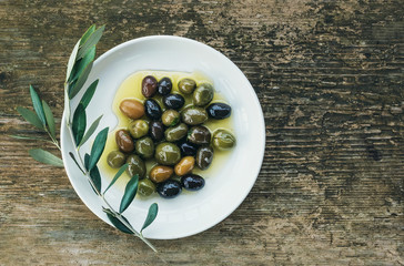 A plate of Mediterranean olives in olive oil with a branch of ol