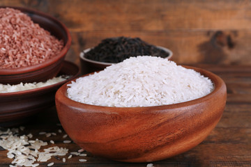 Different kinds of rice in bowls on wooden background