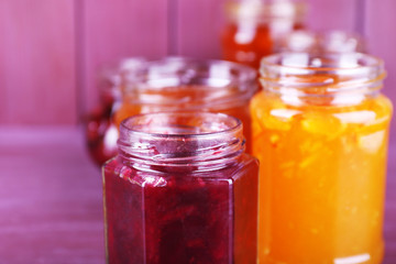 Homemade jars of fruits jam on color wooden background