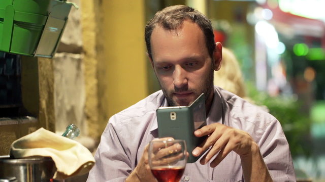 Young man taking photo of food with cellphone and drinking wine 
