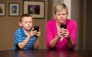 Mother and young son on mobile cell phones texting.