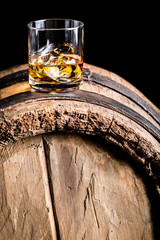 Whiskey glass with ice on old wooden barrel