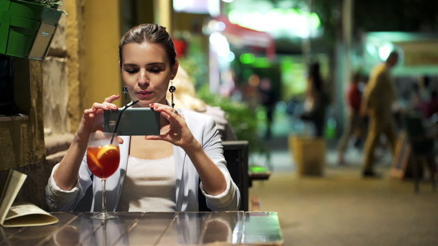 Young woman taking photo of cocktail with cellphone in cafe