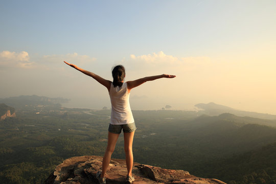 	strong confident woman hiker open arms at on mountain peak rock