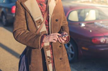 Woman using smart phone next to her car