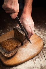 Male hands slicing fresh bread on table