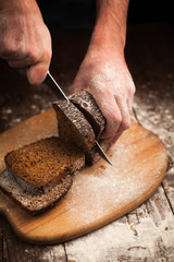 Male hands slicing fresh bread on table