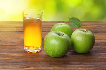 Glass of apple juice and apples on wood