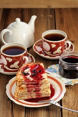 Russian bliny with currant jam, tea cups, pot on wooden backgrou
