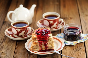 Russian bliny with currant jam, tea cups, pot on wooden backgrou