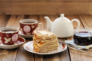 Russian bliny with currant jam, tea cups, pot on wooden backgrou