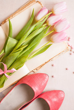 Pink tulips with women`s shoes over white wooden table. Spring c