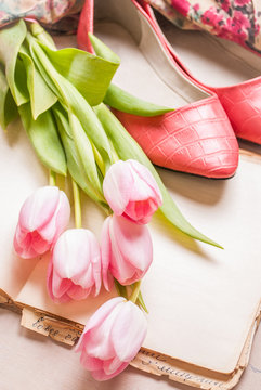 Pink tulips and blank book with women`s shoes over white wooden