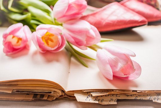Pink tulips and blank book with women`s shoes over white wooden