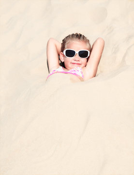 Happy cute little girl lying in sand