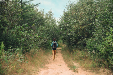 Hiker woman walking on path among trees in summer