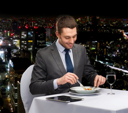 smiling man with tablet pc eating main course