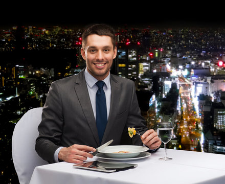 smiling man with tablet pc eating main course