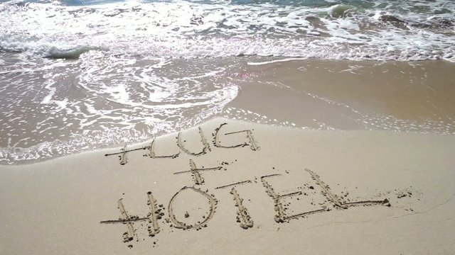 Text FLUG+HOTEL im Sand wird von Wellen weggespült