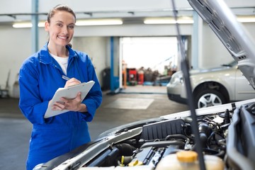 Mechanic smiling at the camera writing on clipboard