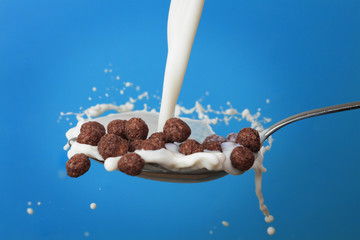 milk splashing into spoon with chocolate cornballs over blue