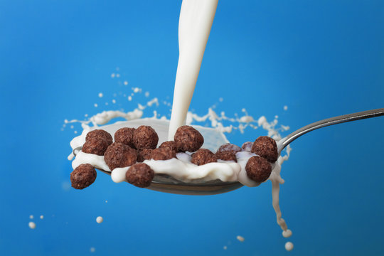 milk splashing into spoon with chocolate cornballs over blue