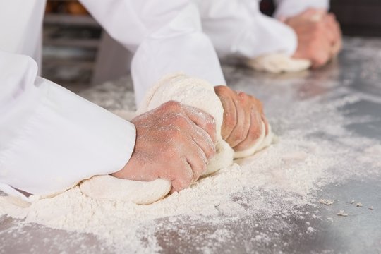 Close up of bakers kneading dough at counter