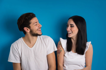 Young couple laughing studio portrait against blue background.