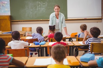 Pretty teacher talking to the young pupils in classroom