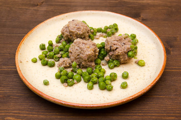 Meatballs with peas on the plate on wooden table
