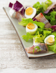 salad with herring, fresh herbs and quail eggs on a  wooden back