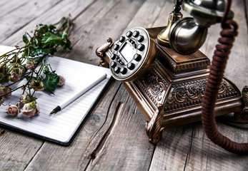 Old vintage black rotary phone and a bouquet of roses on wooden