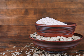 Grains of rice in bowls on wooden background