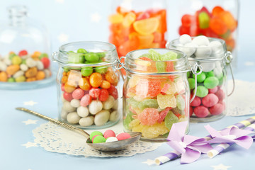 Multicolor candies in glass jars on colorful background